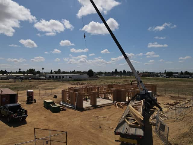 Aerial view of a crane truck lifting roof trusses over the framed walls of a new home on an open lot