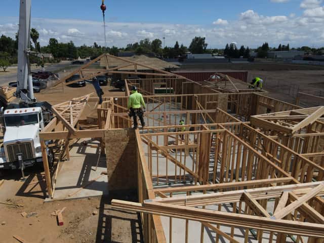 Aerial view over a crane truck and a framer in a hi vis shirt standing on the interior walls as roof trusses go in