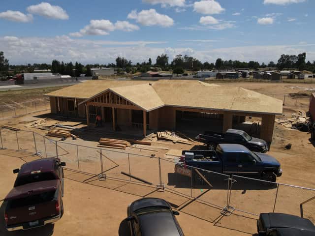 Aerial view of a framed single story home with the roof sheathed, a crane truck and temporary fence in the foreground on a jobsite