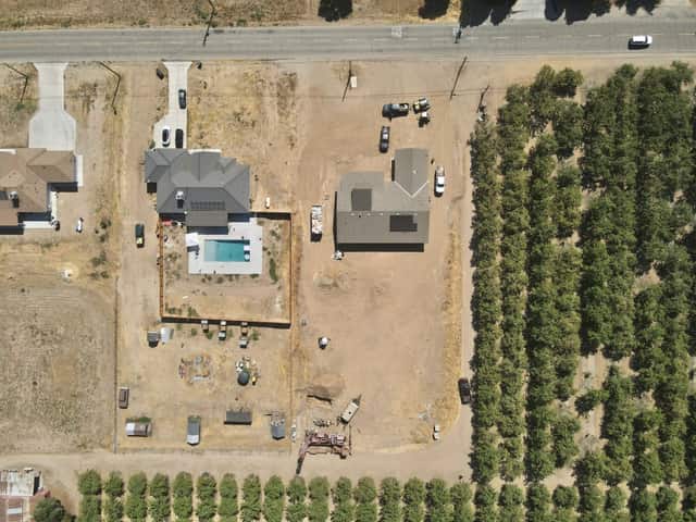 Overhead aerial view of a custom home site with a new swimming pool, bordered by rows of almond trees