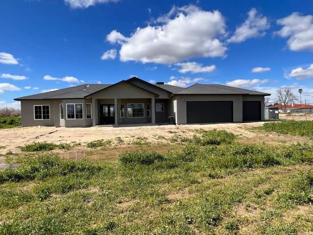 Completed single story home with dark garage doors, seen across a green field