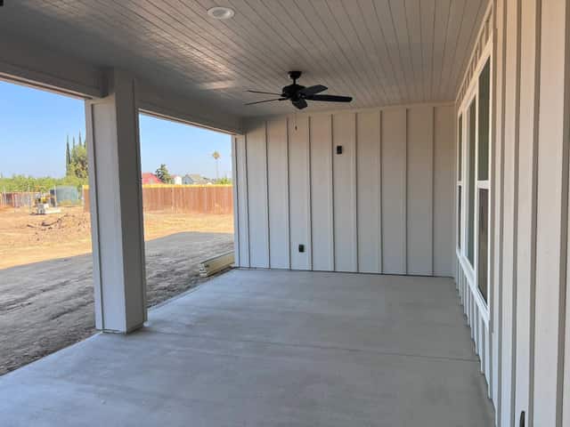 Covered rear patio with a ceiling fan and board and batten siding
