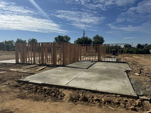 A finished concrete slab in the foreground with framed walls standing on the rest of the foundation behind it