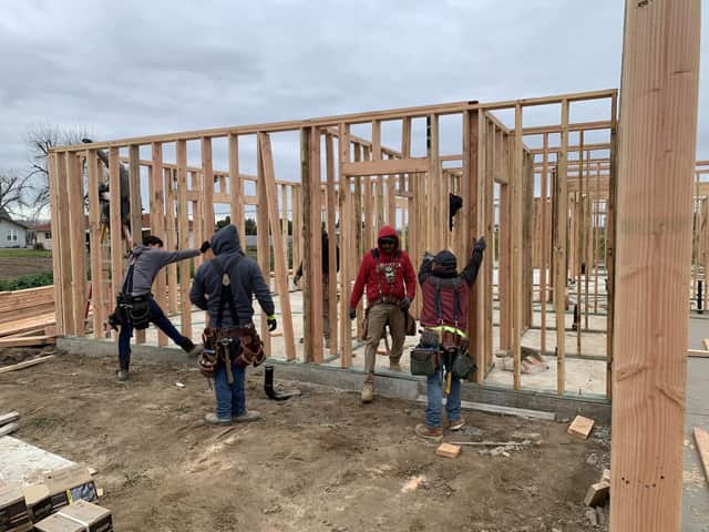 Four framers bracing a standing wall section on the foundation of a new home