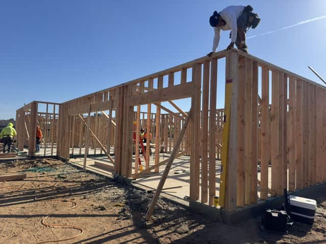 A framer on top of a wall setting the top plate while the rest of the crew works below
