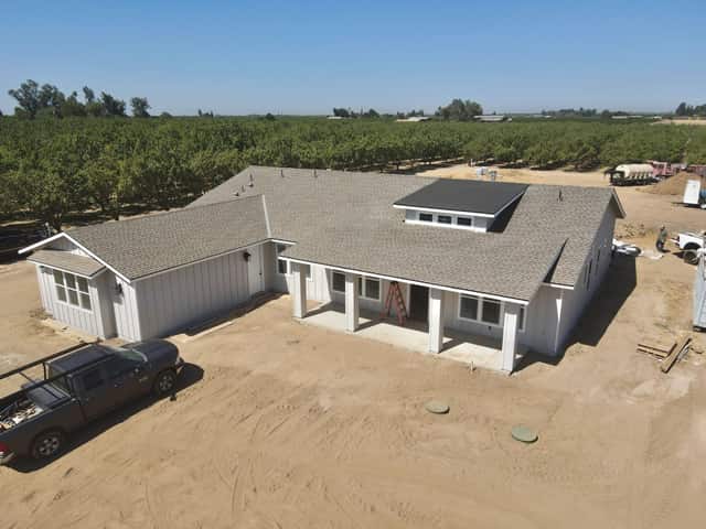Custom home nearing completion on a dirt lot with an almond orchard behind it