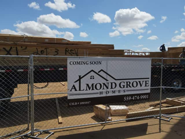 Almond Grove Homes coming soon sign on a chain link fence in front of a flatbed stacked with roof trusses
