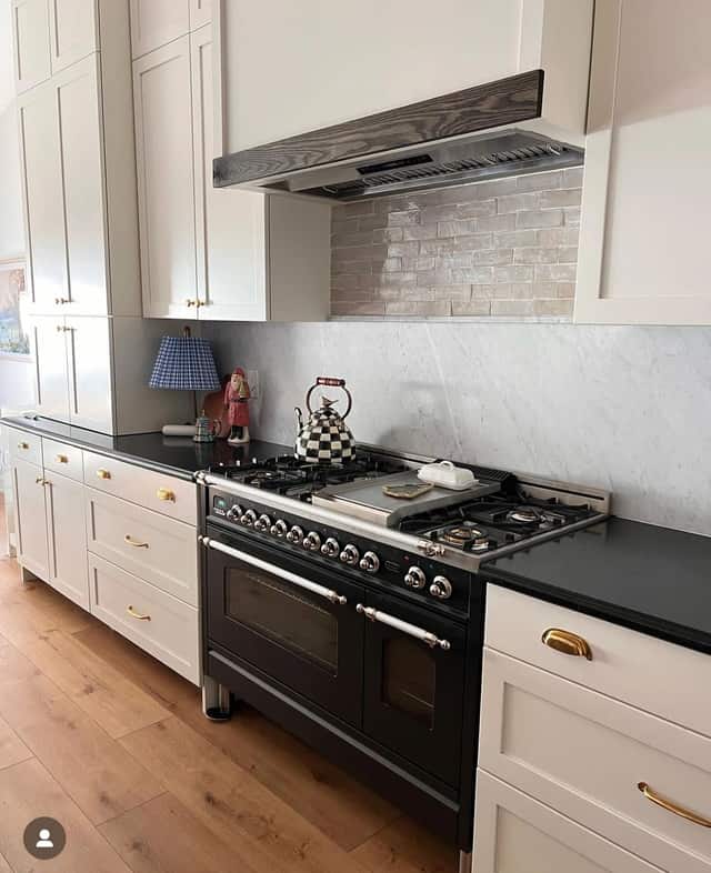Remodeled kitchen with a black professional range, a marble backsplash, and white cabinetry