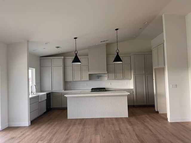 Newly finished kitchen with white cabinets, an island, and black pendant lights, ready for move in