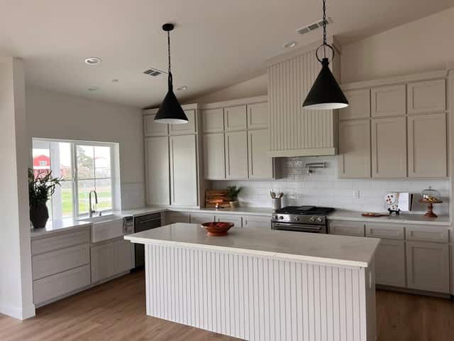 Finished kitchen under a vaulted ceiling with a white island and black pendant lights