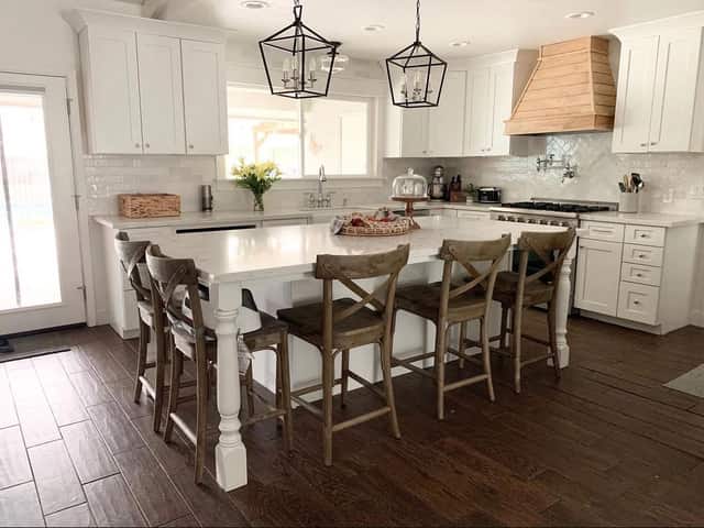 Finished custom kitchen with a large white island, wood bar stools, and a wood range hood