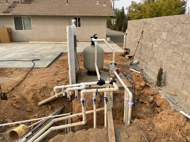 Pool filter and plumbing valves at the equipment pad beside a block wall