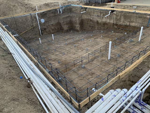 A swimming pool excavation with a full rebar cage, a bench step, and bundled plumbing lines along the edge