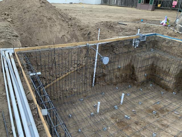 Corner of a pool excavation showing the tied rebar grid, a return fitting, and bundled plumbing lines