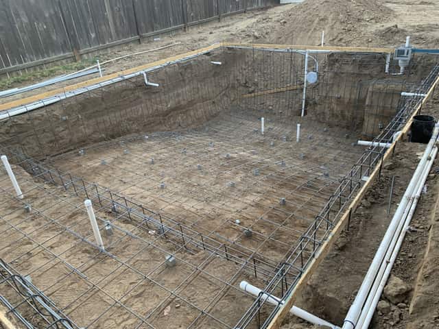 An excavated swimming pool with the rebar cage tied and the plumbing lines set along the edge