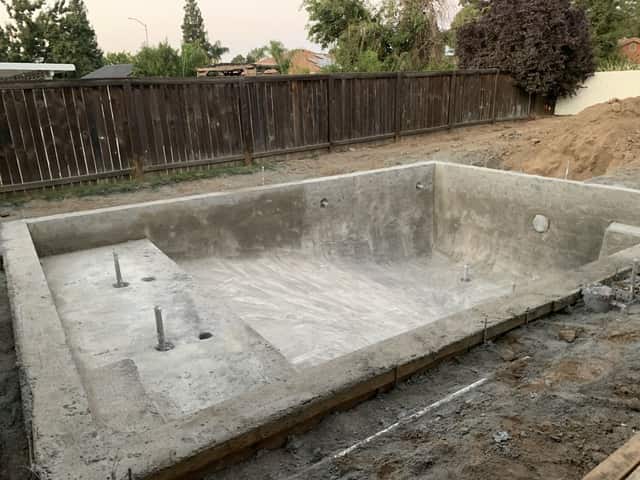 A concrete pool shell with a tanning ledge, steps, and light niches