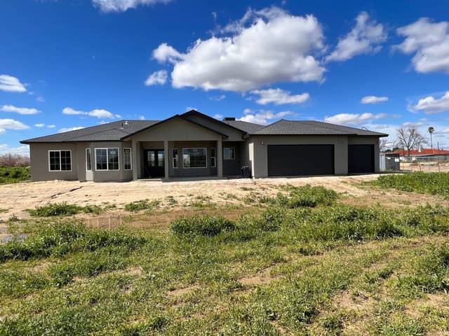 Completed single story home with dark garage doors, seen across a green field. Opens our real estate services page.