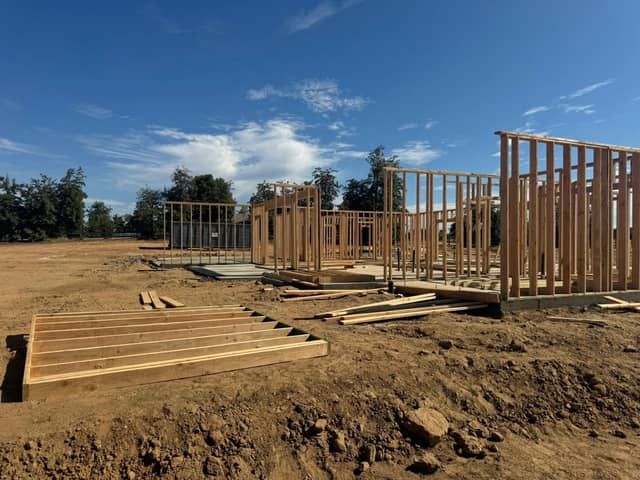 Framed walls standing on a slab with framing lumber stacked on site. Opens our commercial construction page.