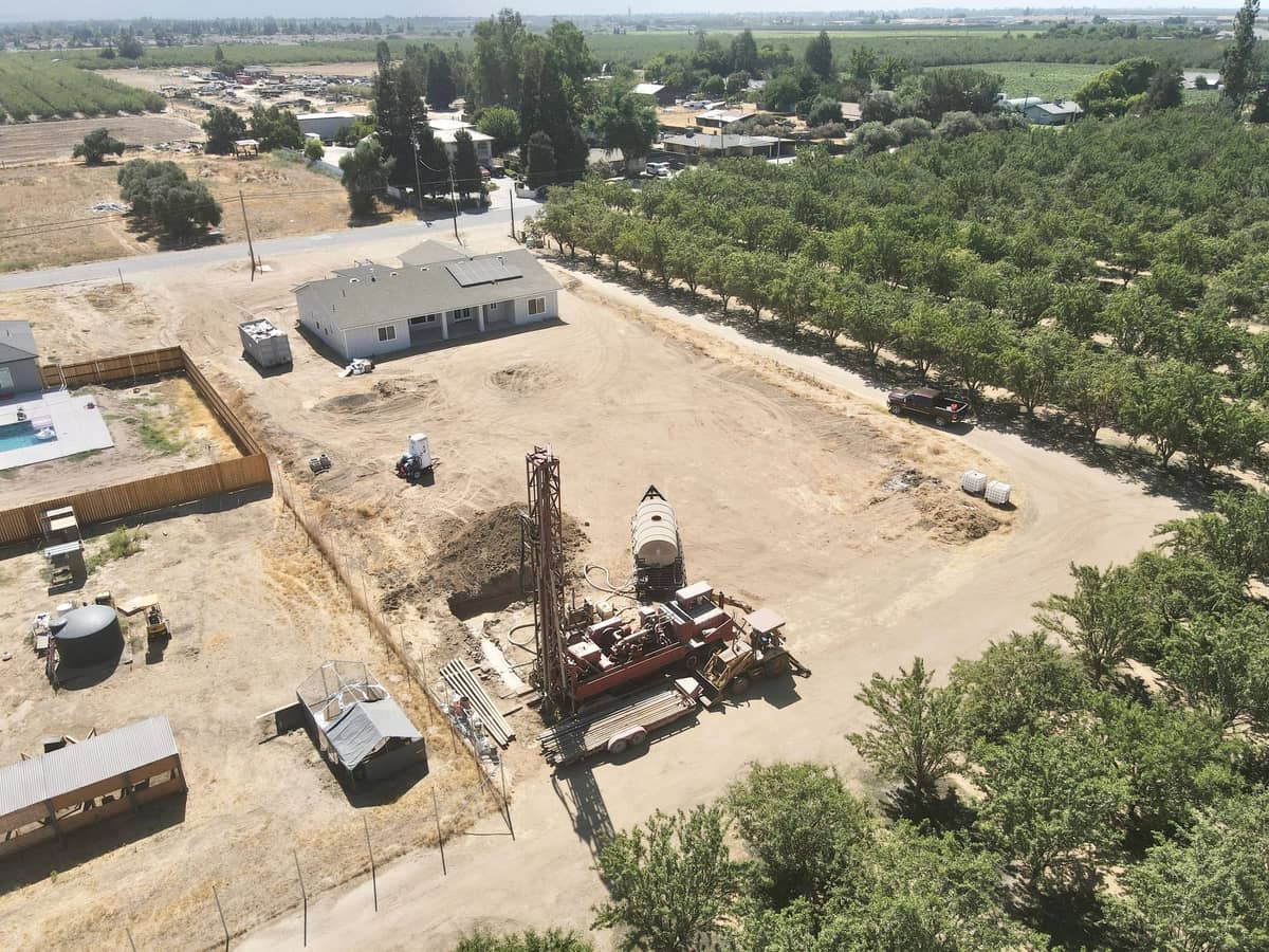 Aerial view of an Almond Grove Homes jobsite with a well drilling rig beside an almond orchard