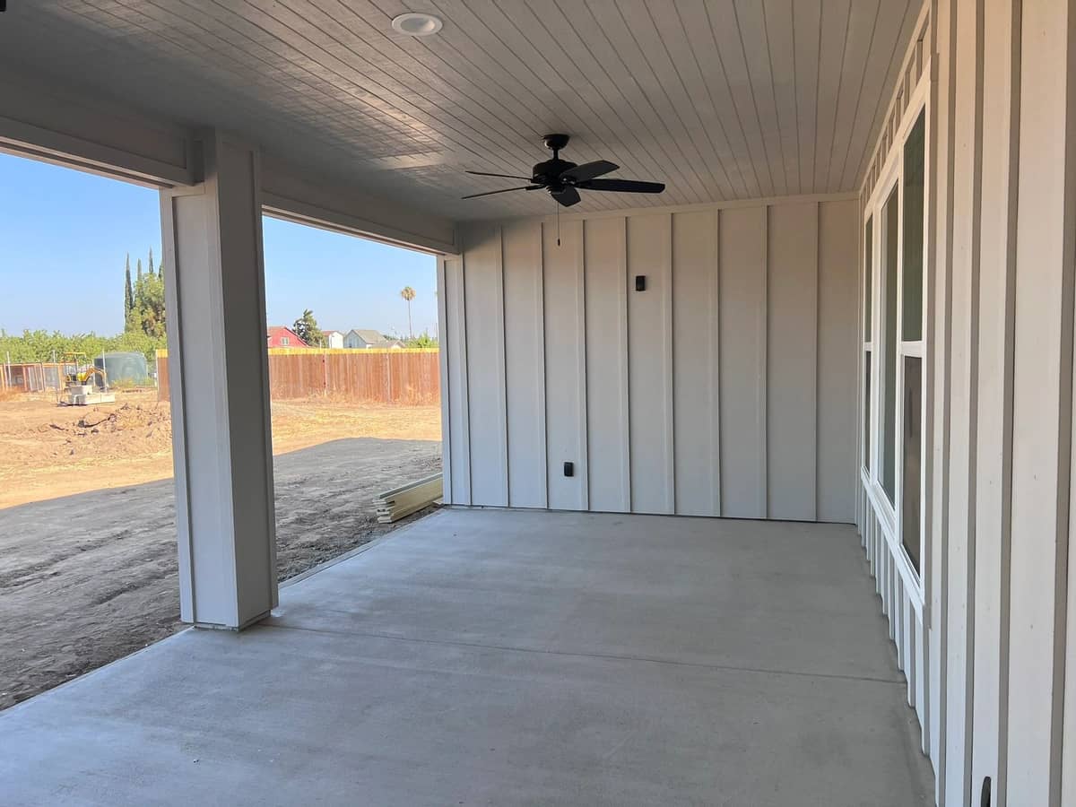 Covered rear patio with a ceiling fan and board and batten siding